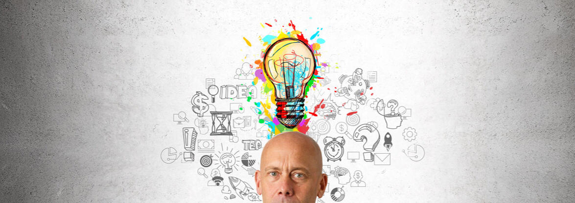 Get In Touch! The image shows a man standing confidently in front of a textured wall with a vibrant, colorful lightbulb illustration above his head. Surrounding the lightbulb are various hand-drawn business-related icons and symbols, emphasizing ideas and creativity. Th
