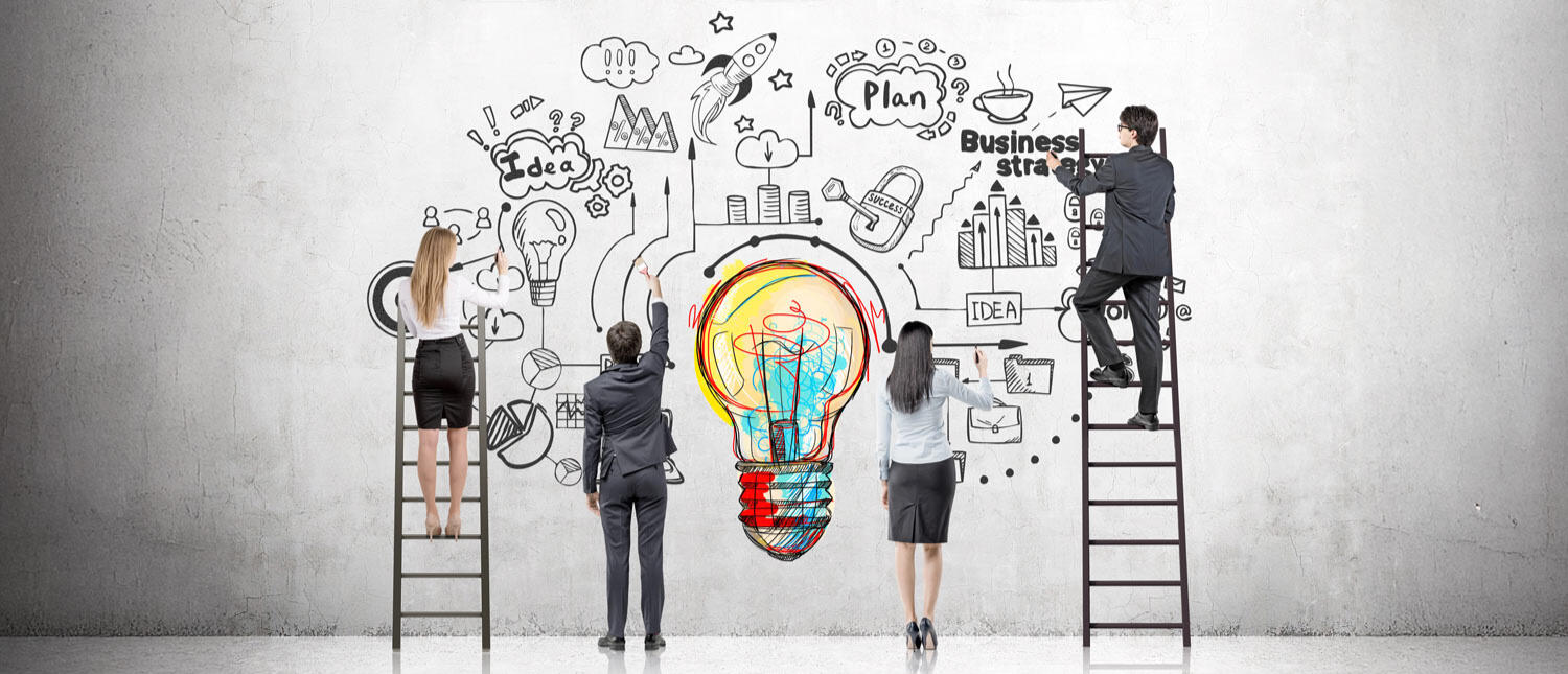 Our mission is to transform businesses by focusing on personal growth, strategic development, and operational excellence. The image shows four professionals collaborating on a large brainstorming illustration on a wall. Two individuals, dressed in formal attire, stand on ladders while two others work from the ground. The wall features a vibrant lightbulb design surrounded by